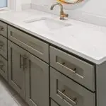 Close-up of an olive green vanity with white marble countertop, brass faucet, and brass hardware.