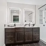 Bathroom remodel with dark wood double vanity, backlit LED mirrors, and dramatic marble backsplash.