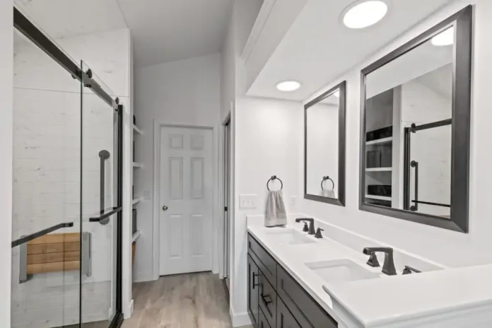 Bathroom remodel with dark double vanity, black-framed mirrors, glass shower with wood bench, and built-in linen shelving.