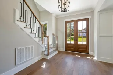 Home entryway with medium-tone hardwood floors, a stained wood double front door with glass panes, and a modern open-rail staircase with black metal balusters.