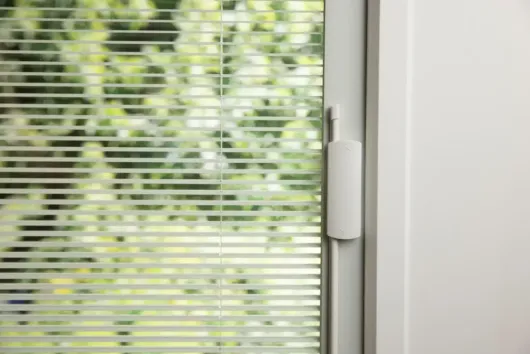 A close-up view of a glass window or door featuring white blinds enclosed between the panes of glass.