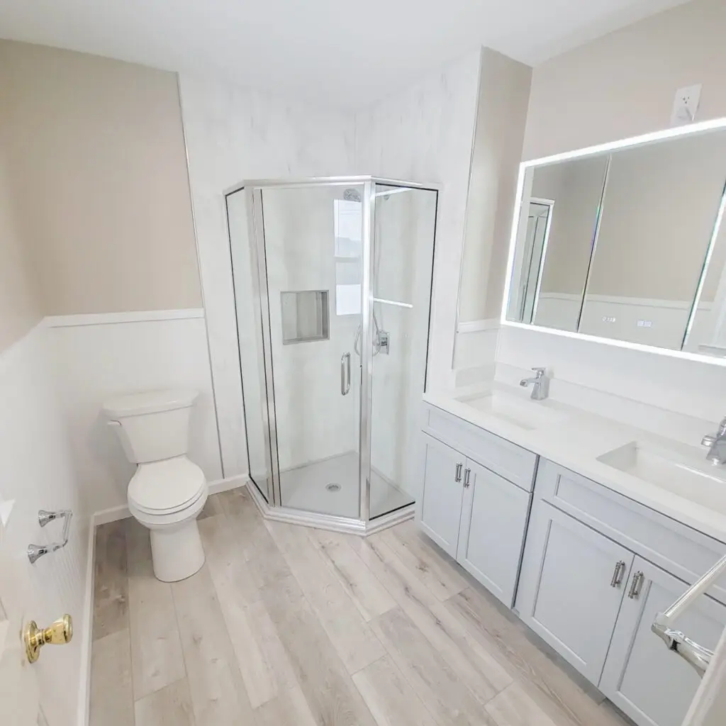 Bathroom remodel with corner glass shower, light gray double vanity, and backlit LED mirror.