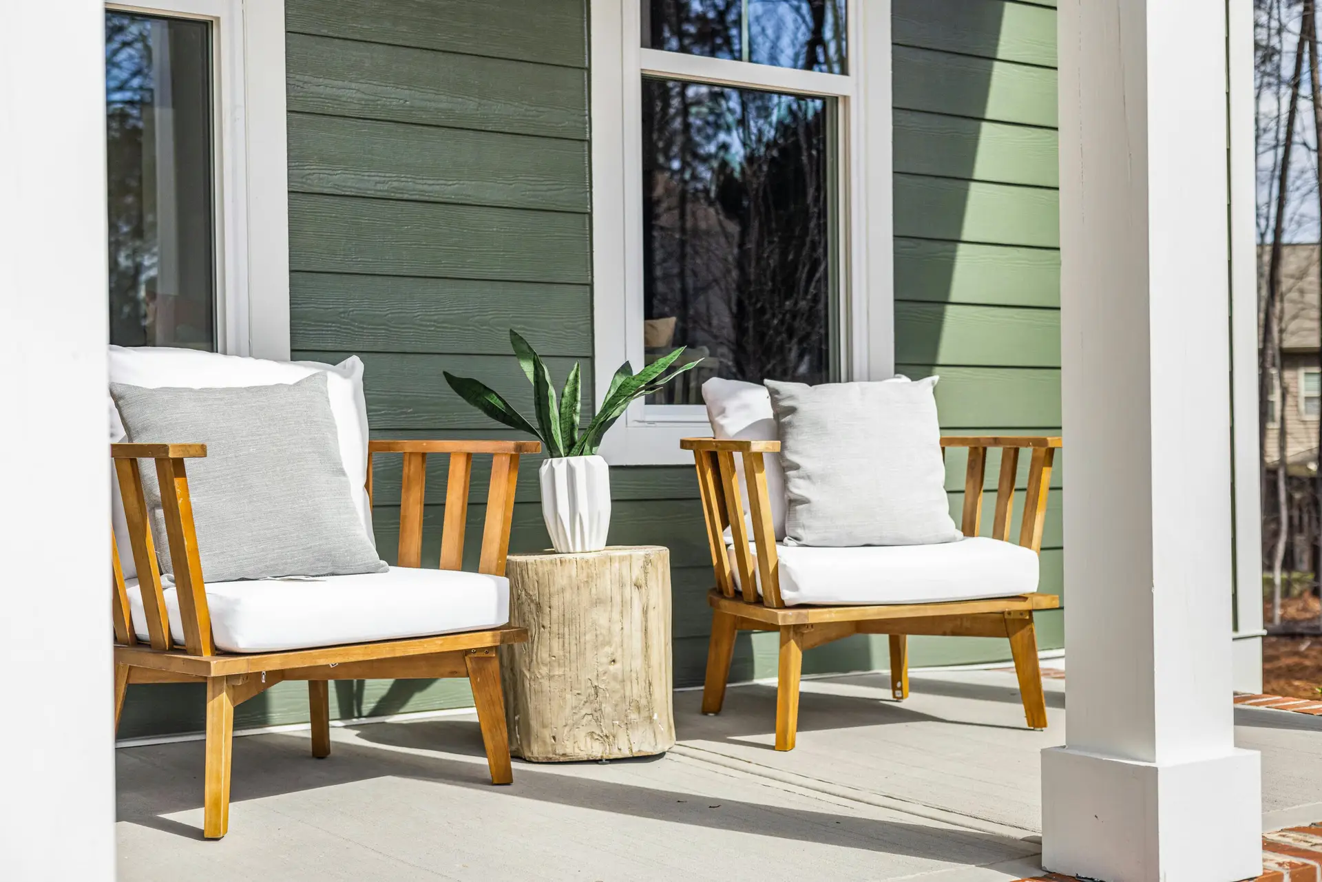 Wooden front porch armchairs with white cushions against olive green siding.