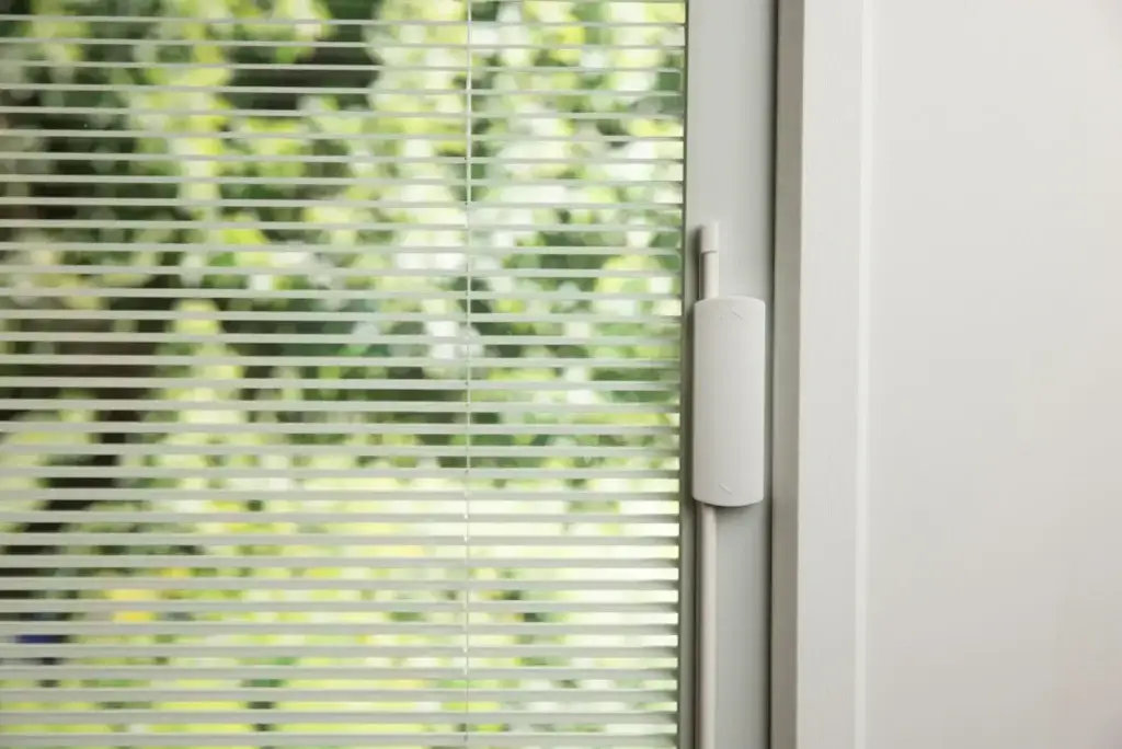 A close-up view of a glass window or door featuring white blinds enclosed between the panes of glass.