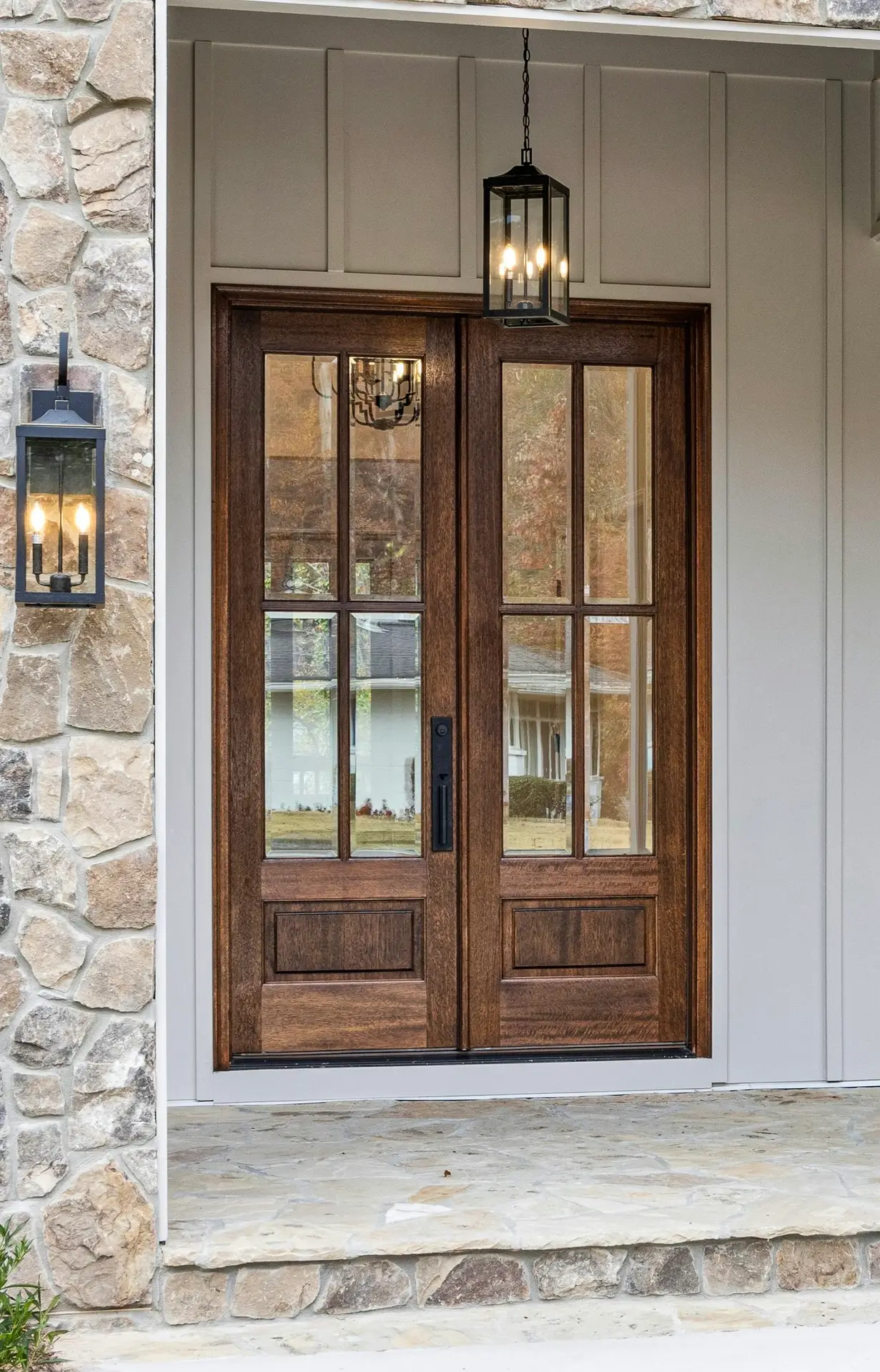Stained wood double front doors with glass panes and black lantern hardware.