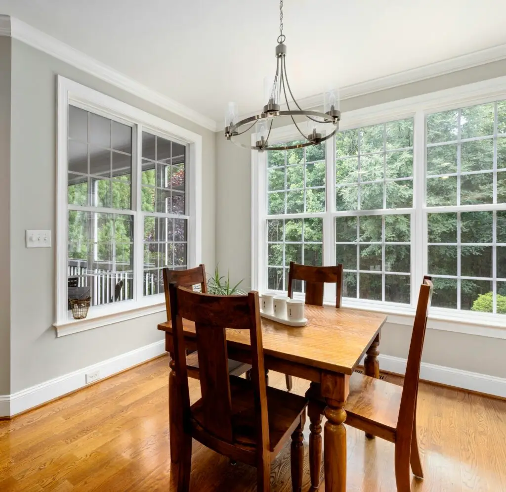 Dining room featuring a wooden table set surrounded by large white windows with grid patterns.
